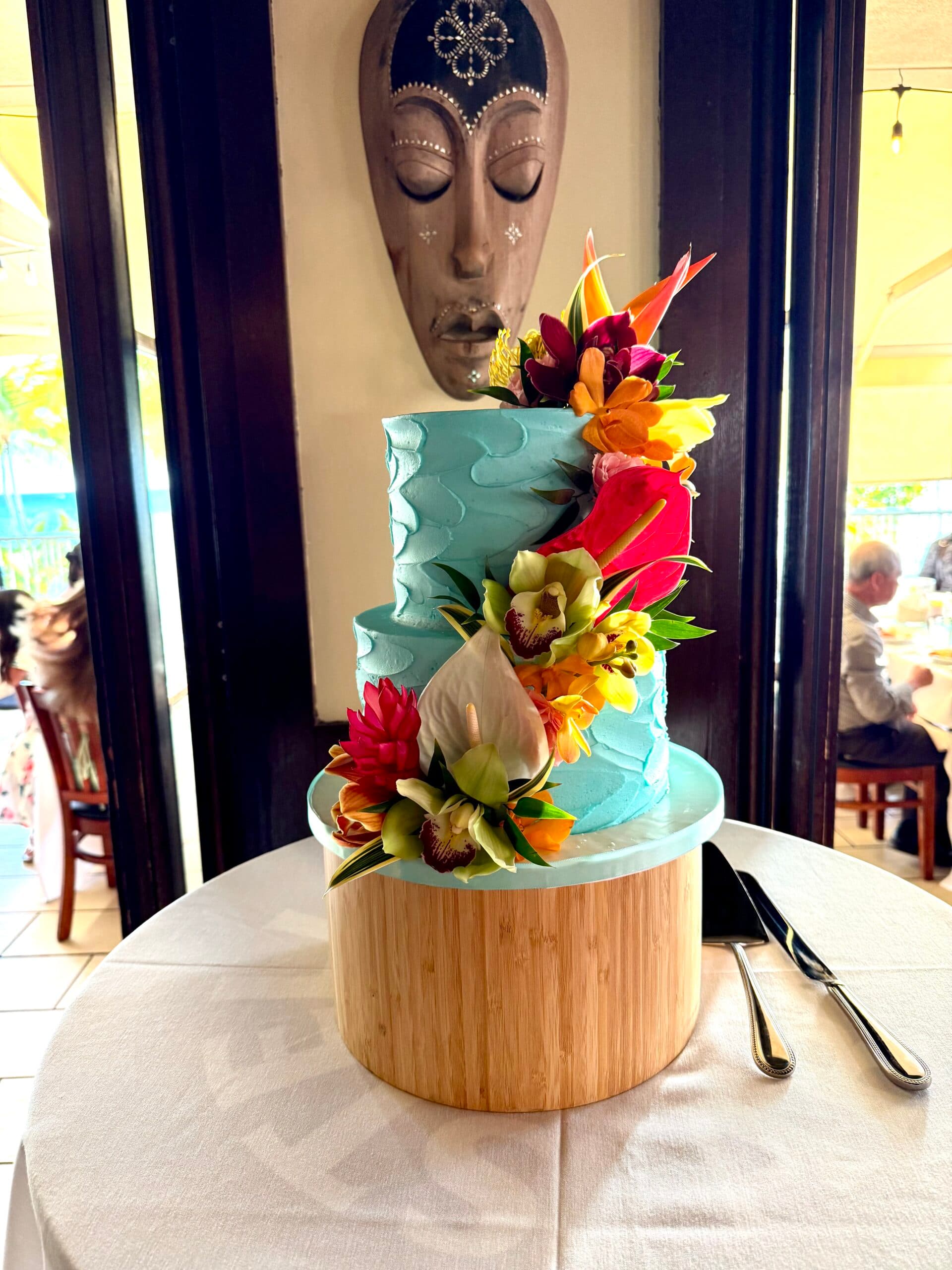 Two-tier tropical wedding cake with turquoise frosting and fresh Hawaiian flowers at Tiki’s Grill & Bar Ocean Room in Waikiki