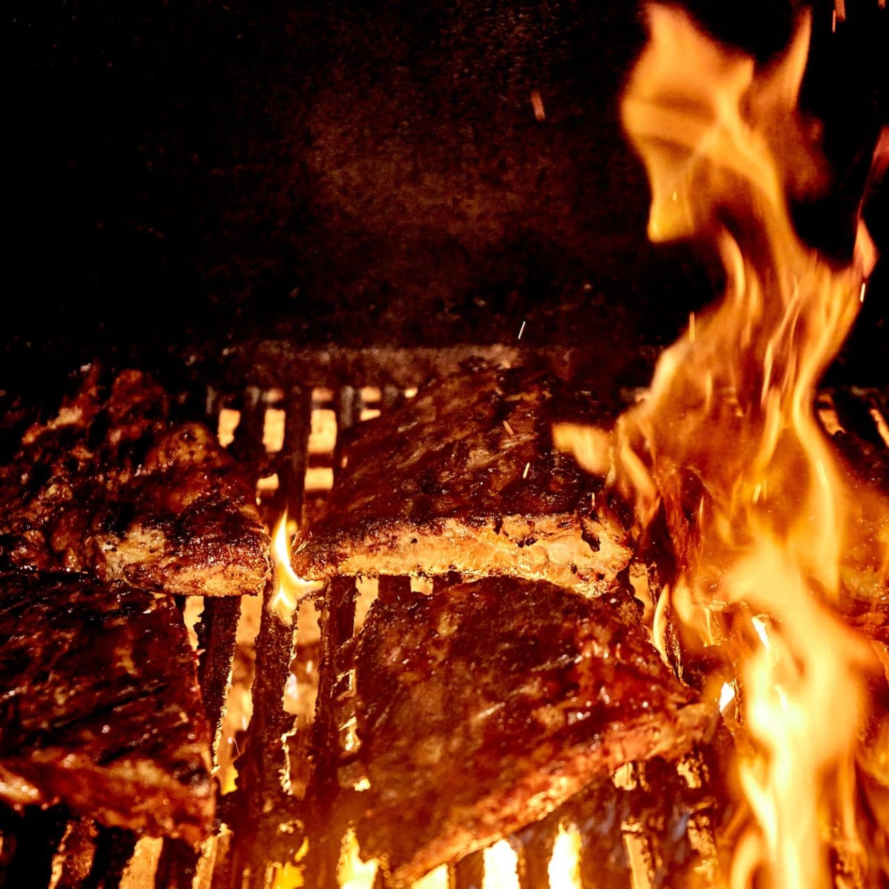 BBQ ribs and a steak being grilled over an open flame, highlighting the restaurant's commitment to quality meats on its menu page.