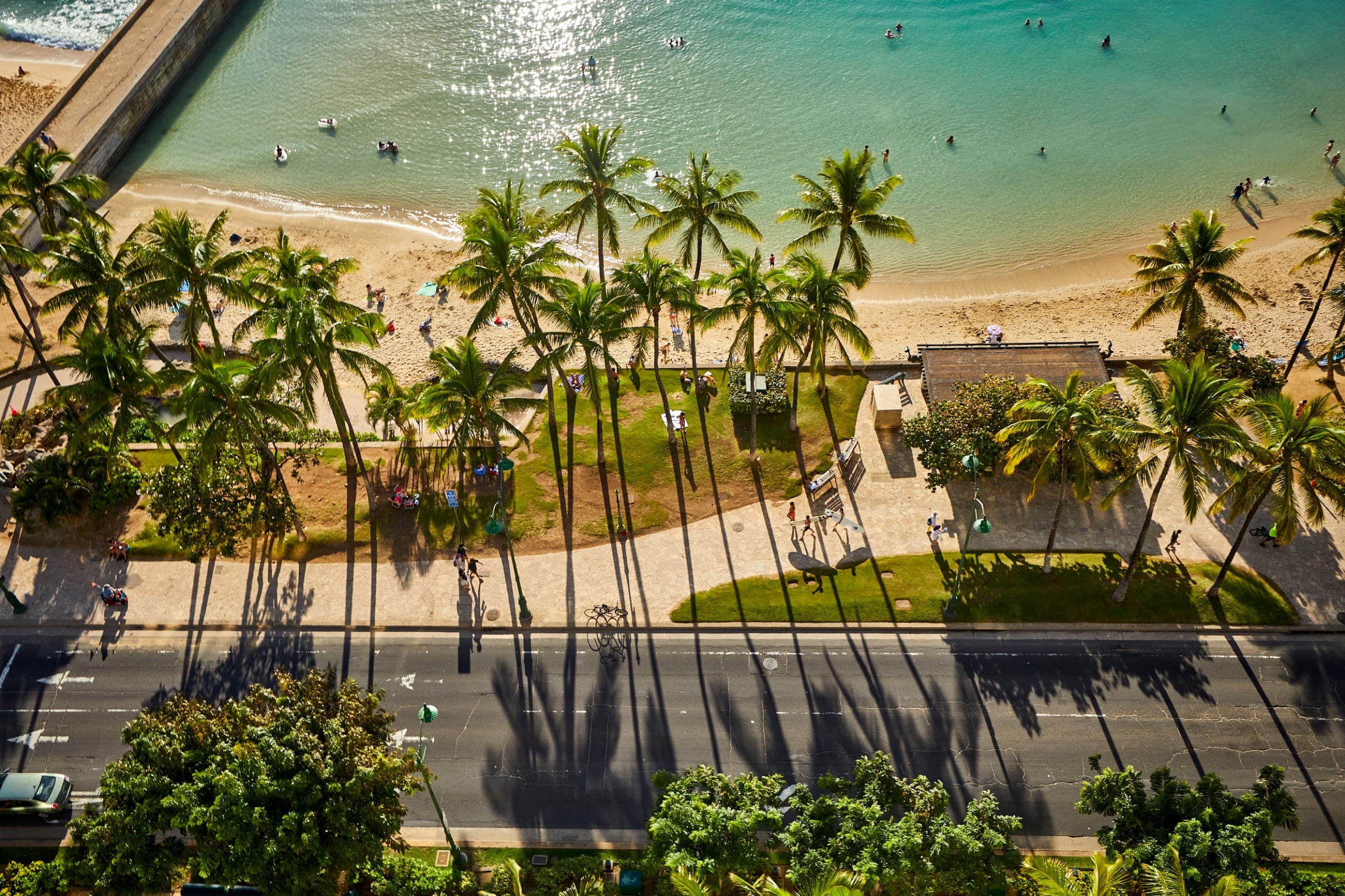 A photo of the Waikiki Walls, with a view of the ocean, inviting guests to visit then come up to Tiki's Grill & Bar for lunch or dinner.