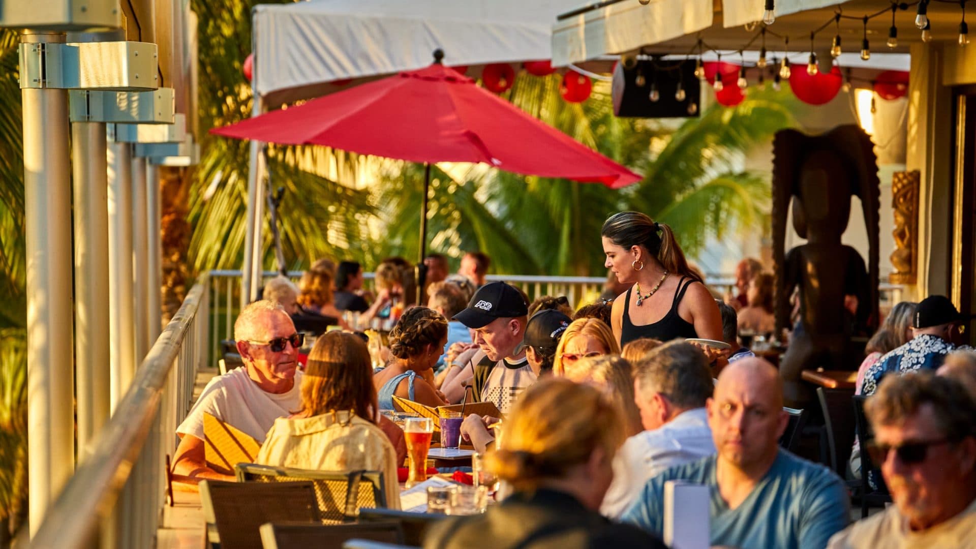 A large group of people having fun and enjoying dinner on the outdoor lanai at Tiki's Grill & Bar, with a focus on their celebration.