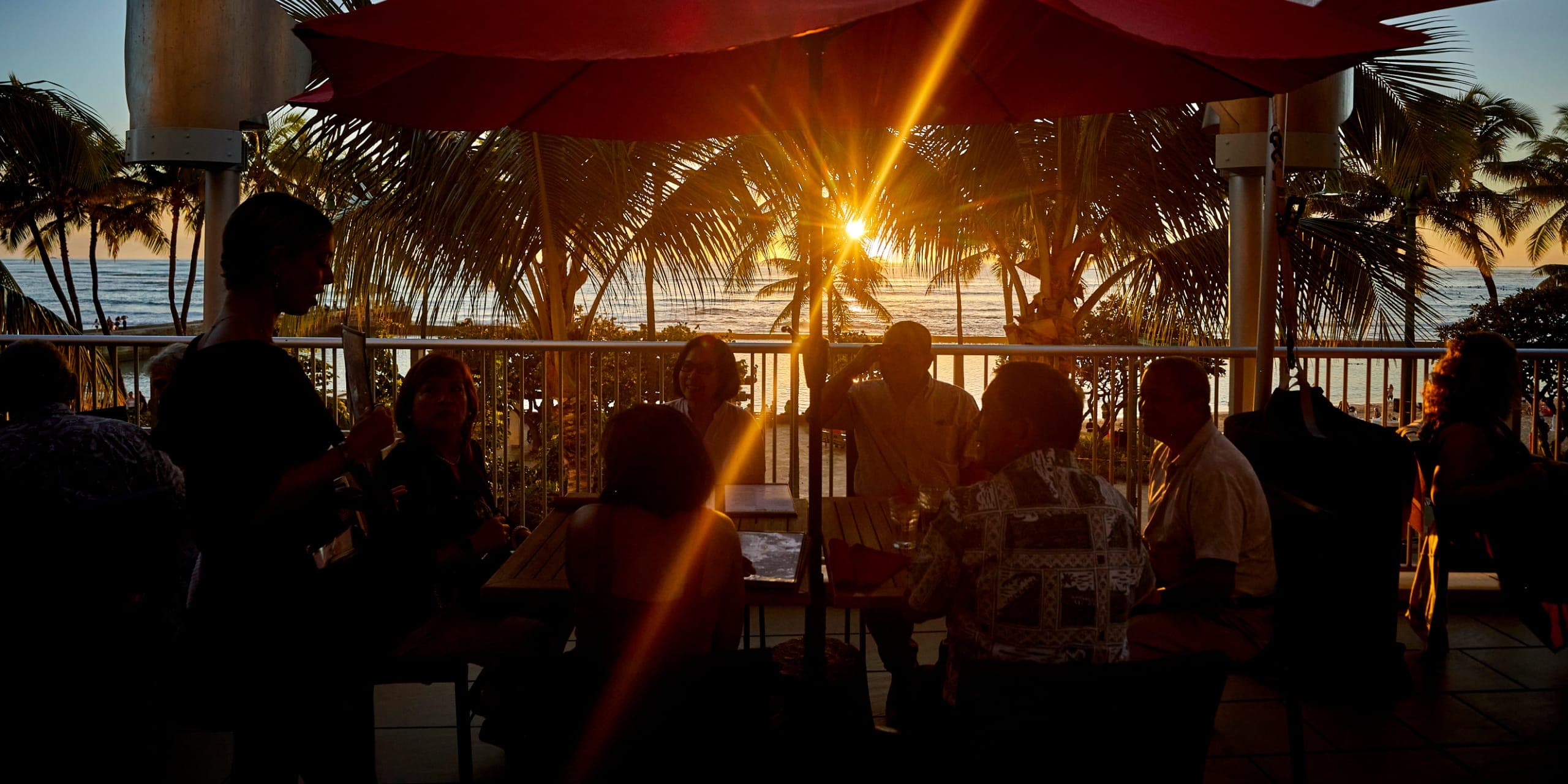 A vibrant sunset photo with guests having fun outside at Tiki's Grill & Bar, enjoying the golden hour and the ocean view.