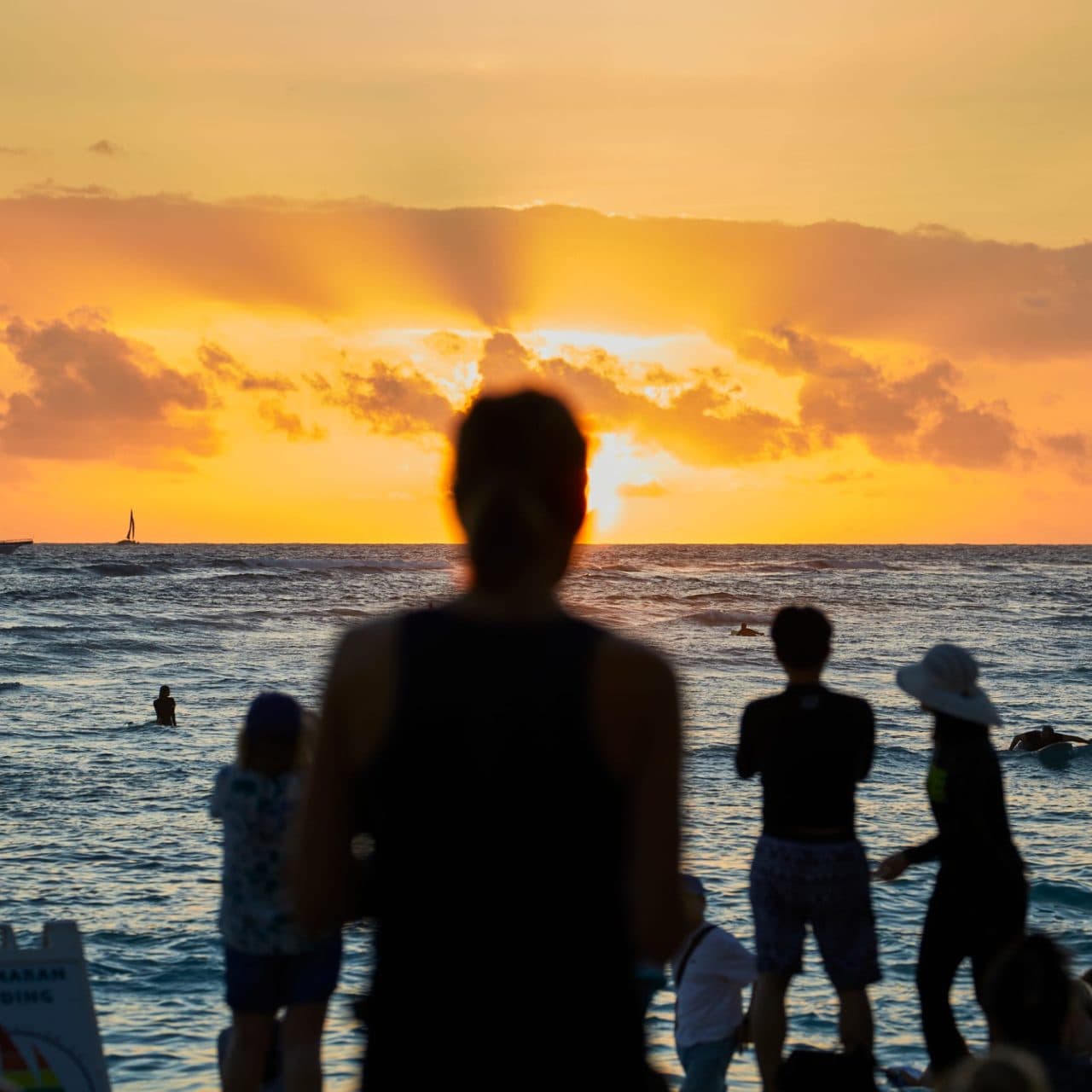 Surfer riding a wave at sunset in Waikiki, viewed from the oceanfront lanai at Tiki’s Grill & Bar, a beachfront restaurant in Hawaii.