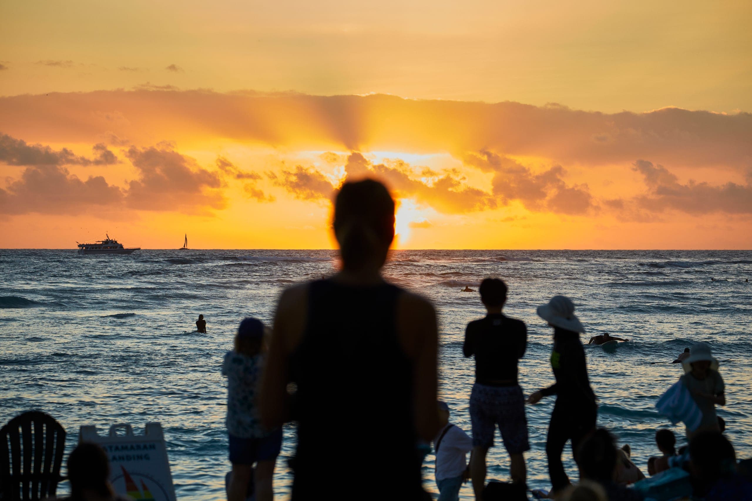Surfer riding a wave at sunset in Waikiki, viewed from the oceanfront lanai at Tiki’s Grill & Bar, a beachfront restaurant in Hawaii.