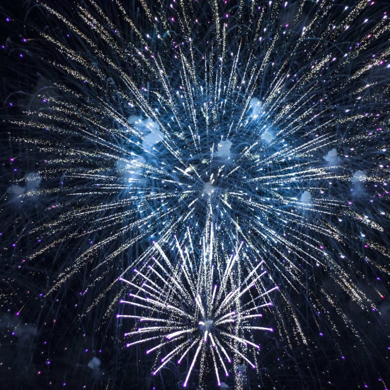 Fireworks exploding in the sky above Tiki's Grill & Bar and the Waikiki coastline at night.