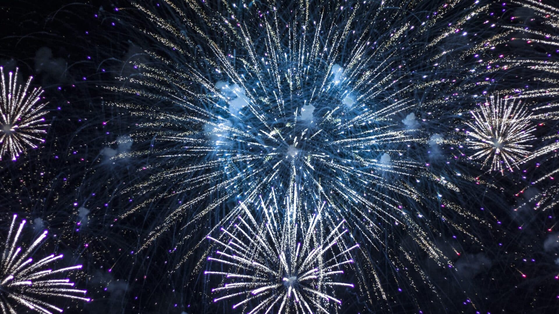Fireworks exploding in the sky above Tiki's Grill & Bar and the Waikiki coastline at night.