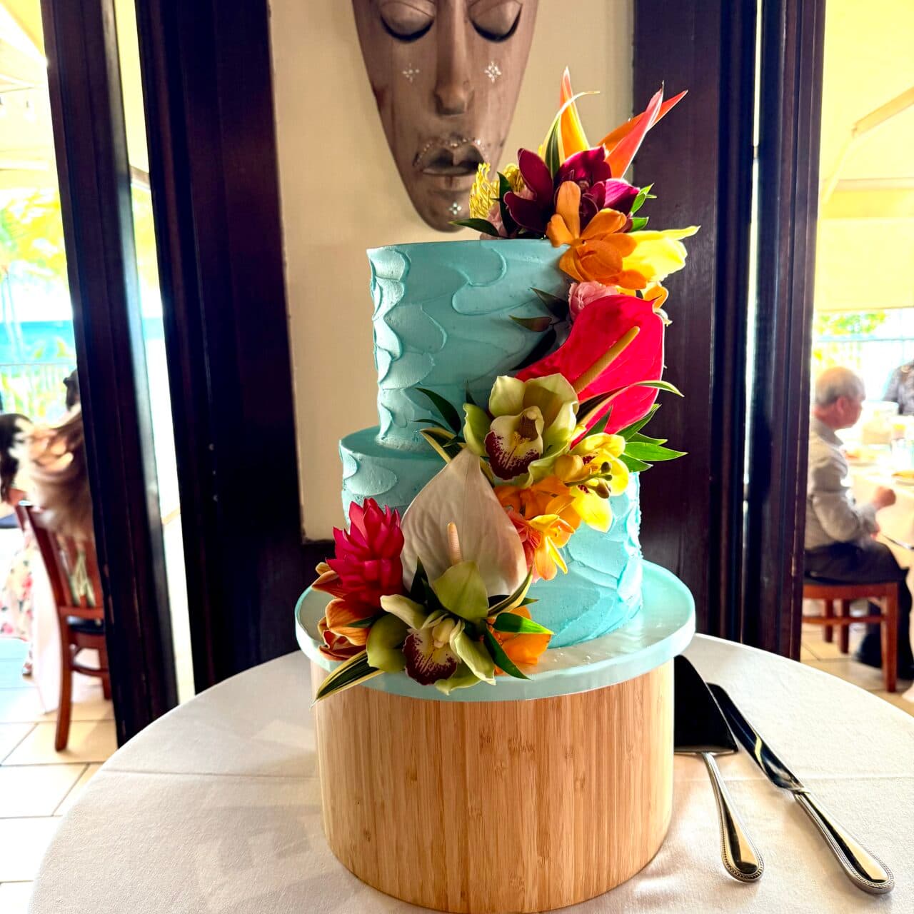 Two-tier tropical wedding cake with turquoise frosting and fresh Hawaiian flowers at Tiki’s Grill & Bar Ocean Room in Waikiki