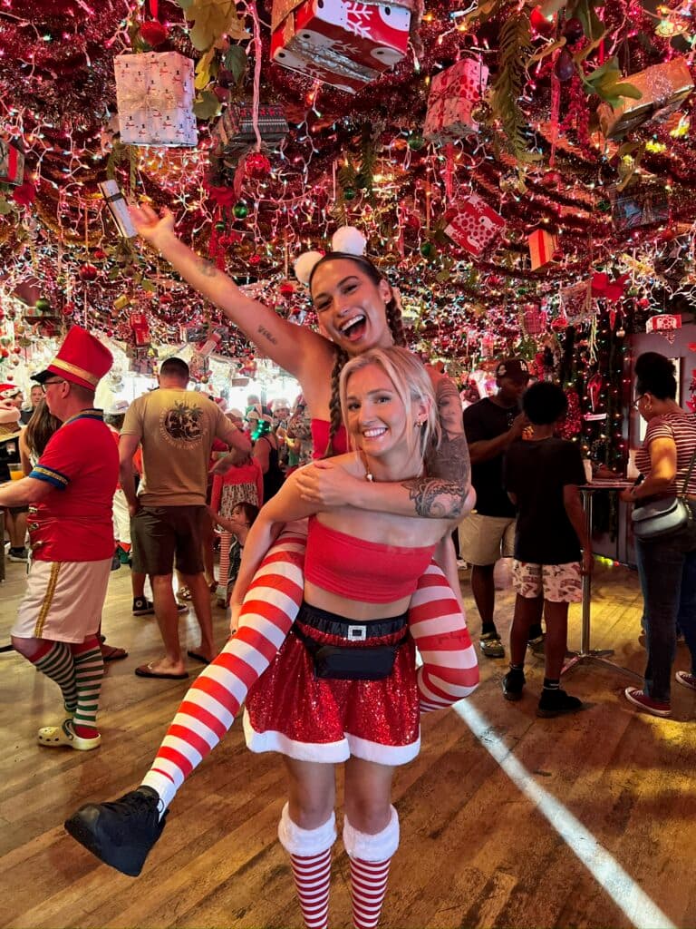 Two playful elves enjoying holiday drinks inside a Christmas themed bar in Honolulu Hawaii surrounded by festive decorations.